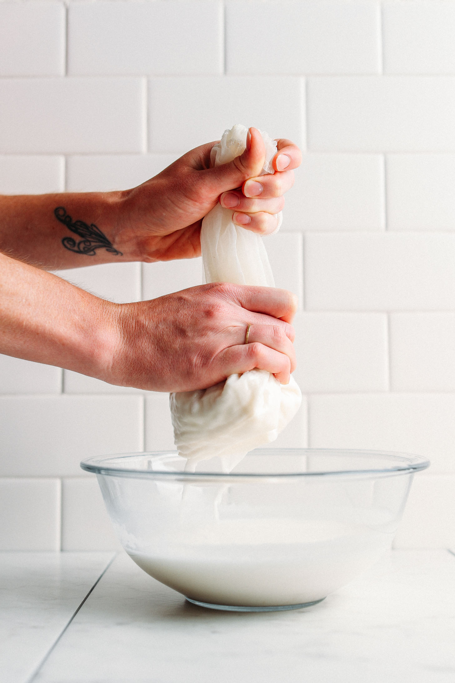 Squeezing homemade nut milk through a nut milk bag into a large bowl