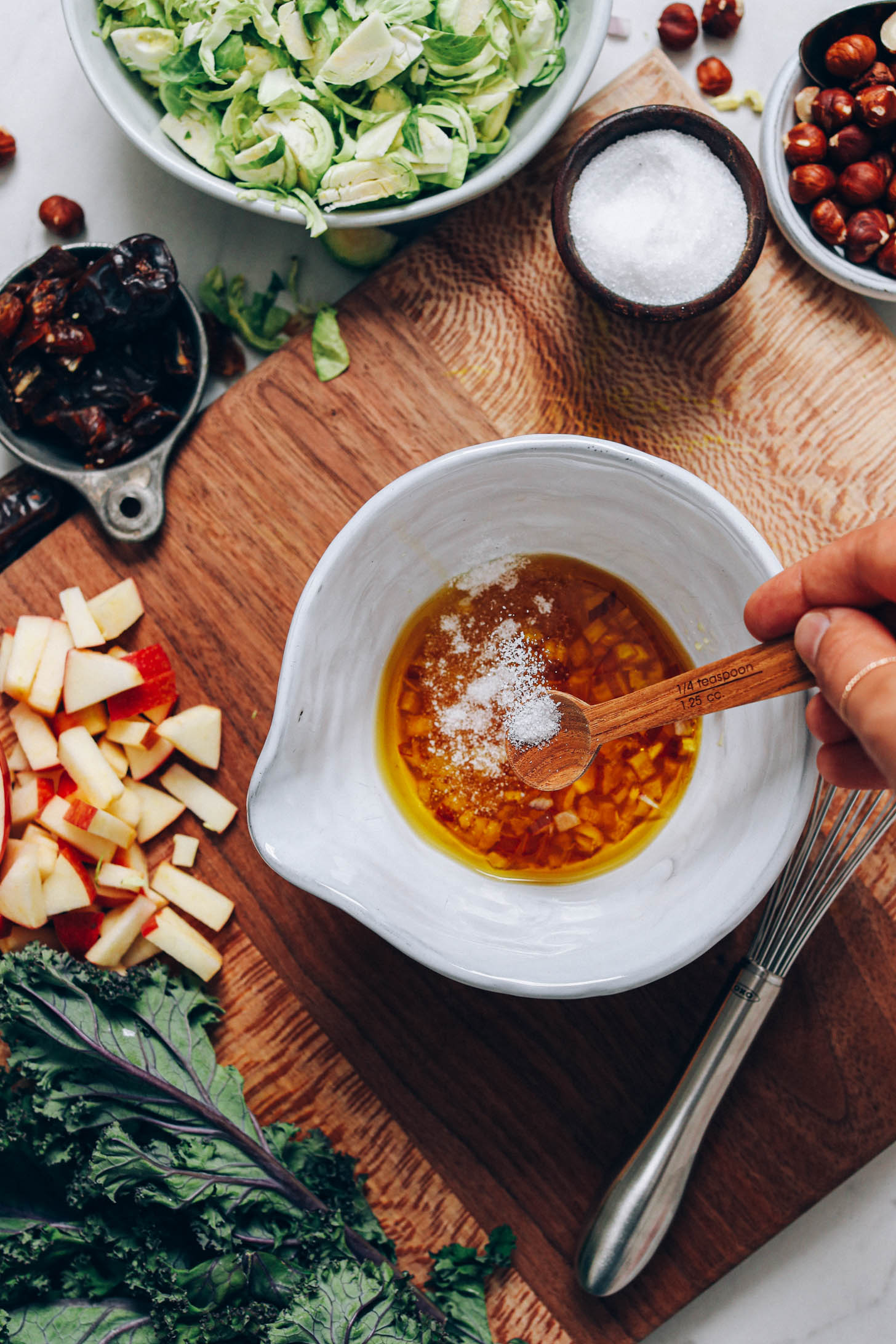 Adding salt to a bowl with olive oil, apple cider vinegar, maple syrup, and shallot