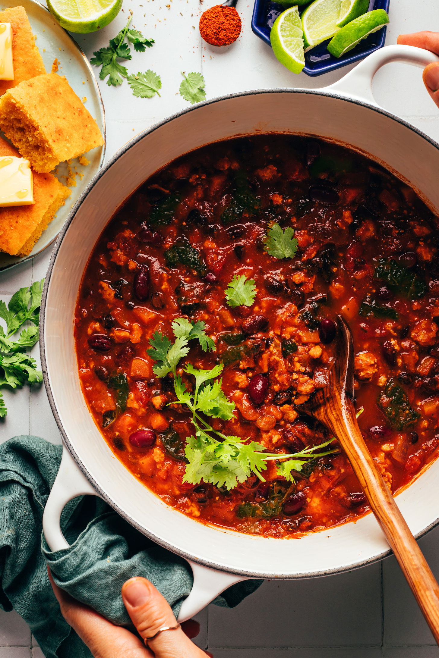 Sliced cornbread next to a pot of pumpkin turkey chili topped with cilantro