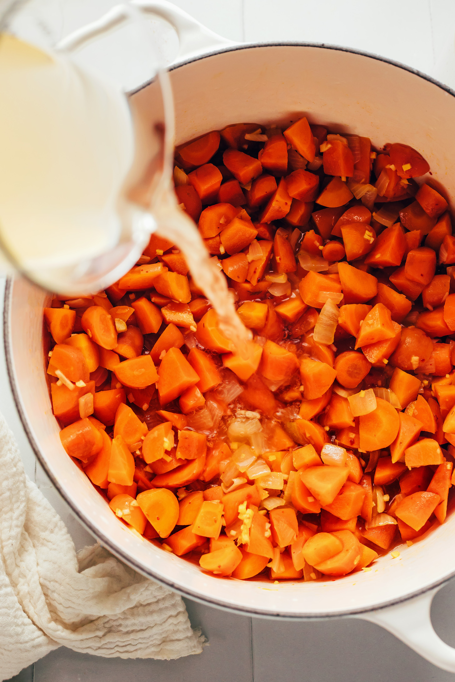 Pouring vegetable broth into a pot of carrots