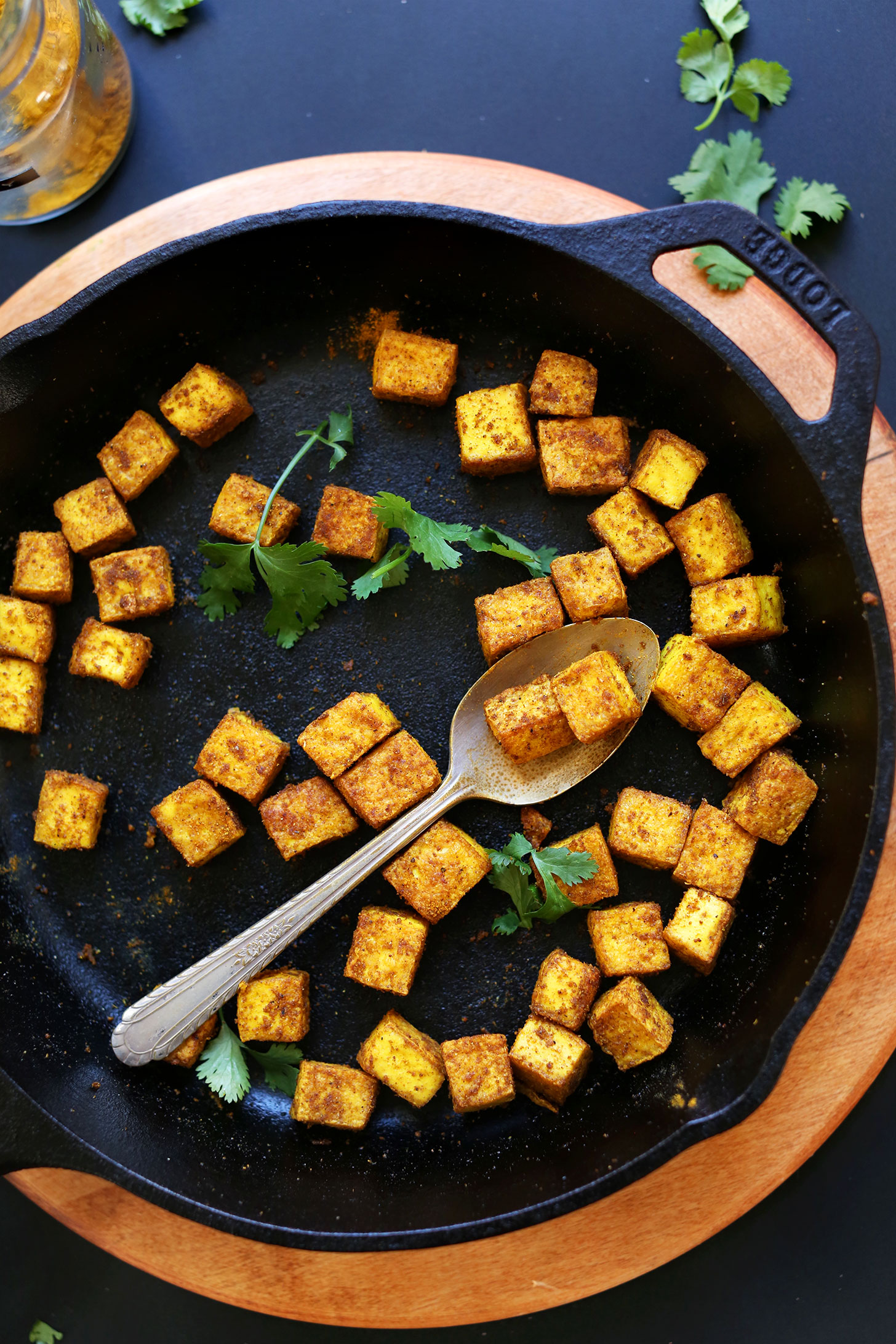 Grabbing a spoonful of Crispy Tofu from a skillet for an easy plant-based meal