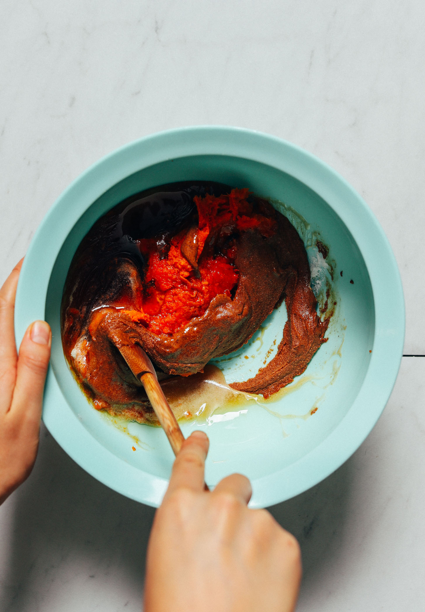 Using a wooden spoon to stir a bowl of Sweet Potato Brownie batter