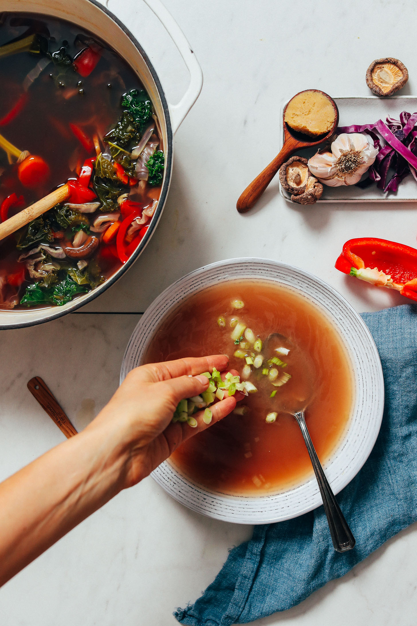 Sprinkling green onions into homemade vegetable broth to make a miso tonic