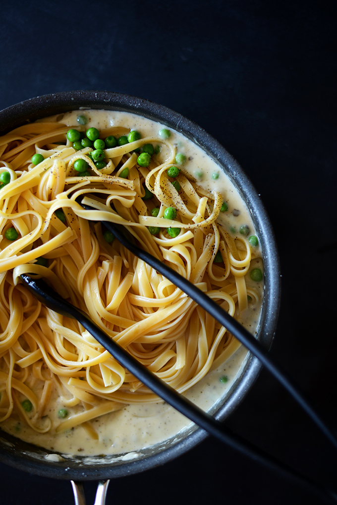 Using tongs to grab a serving of Healthy Alfredo Pasta with Peas