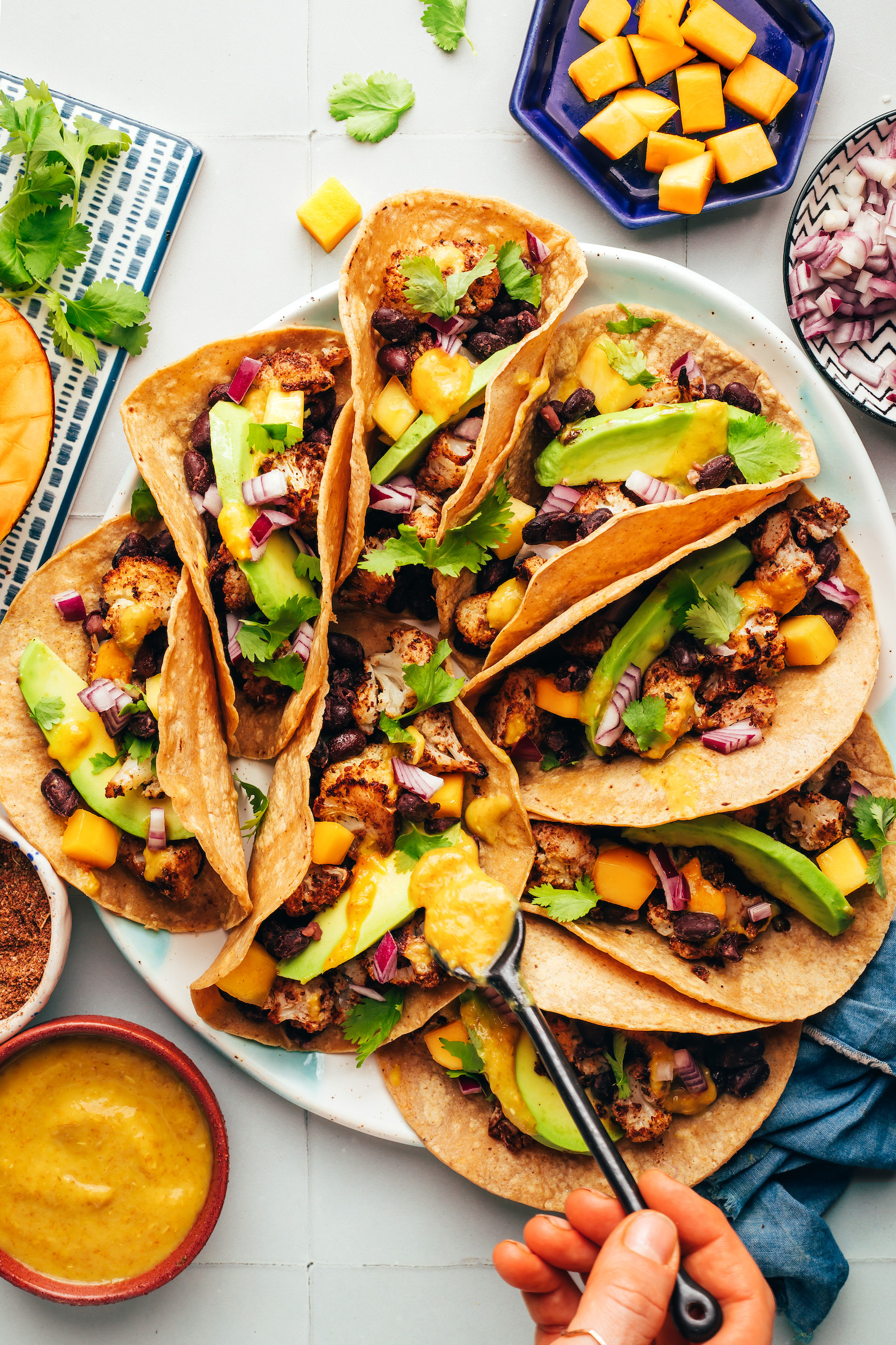 Drizzling mango hot sauce onto a taco on a platter of jerk cauliflower tacos