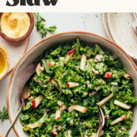 Serving utensils in a bowl of kale apple slaw