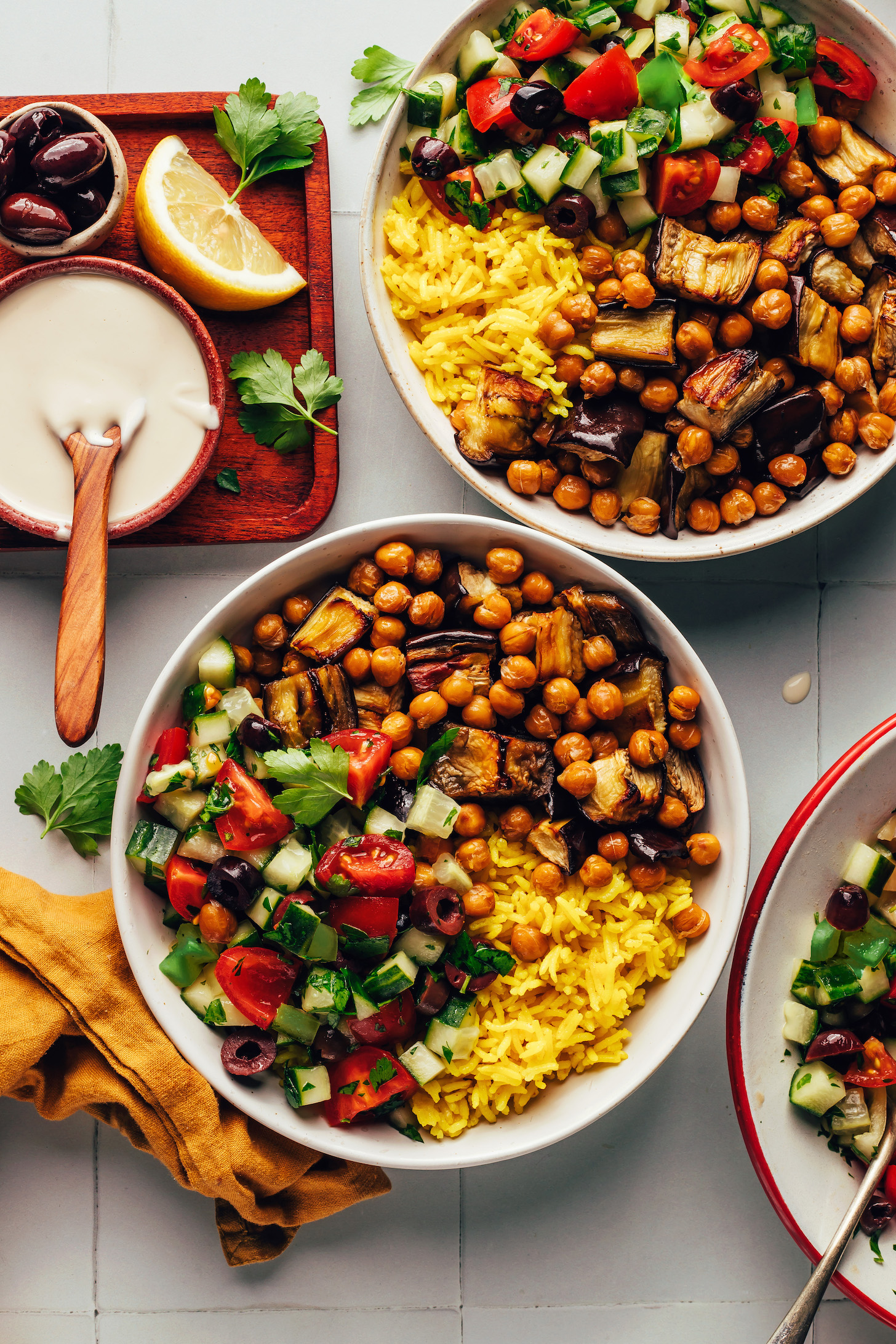 Tahini sauce, lemon, parsley, and olives next to two Mediterranean-inspired chickpea nourish bowls