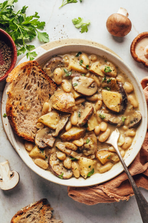 Crusty sliced bread in a bowl of white bean mushroom stew