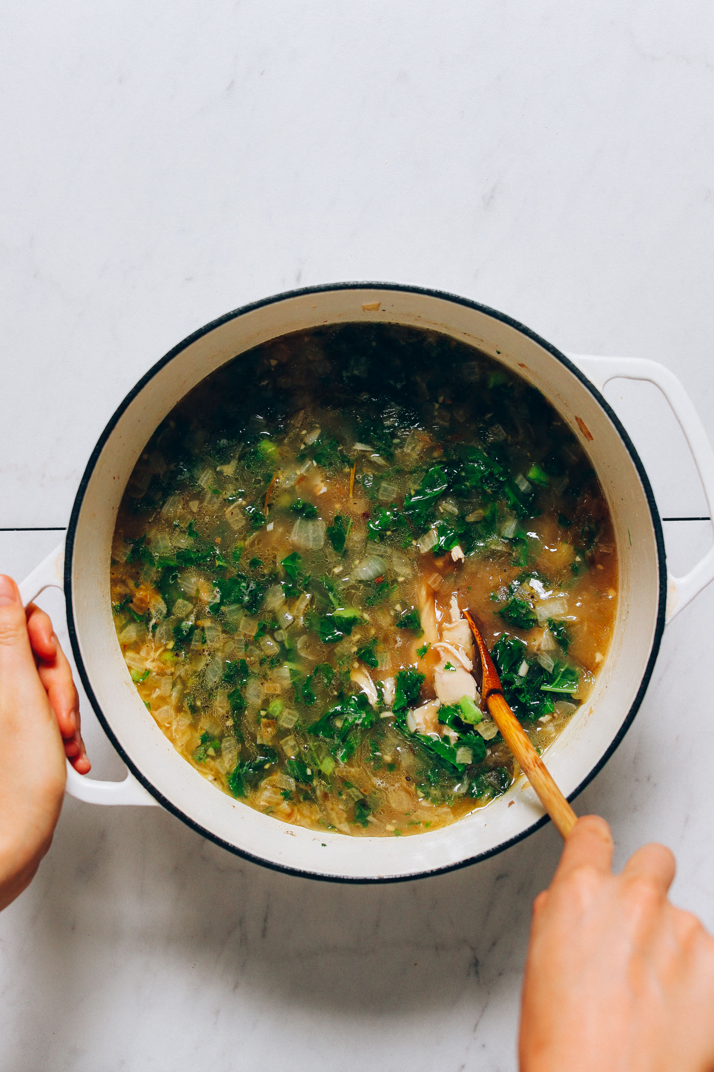 Using a wooden spoon to stir a pot of White Bean Kale Chicken Soup