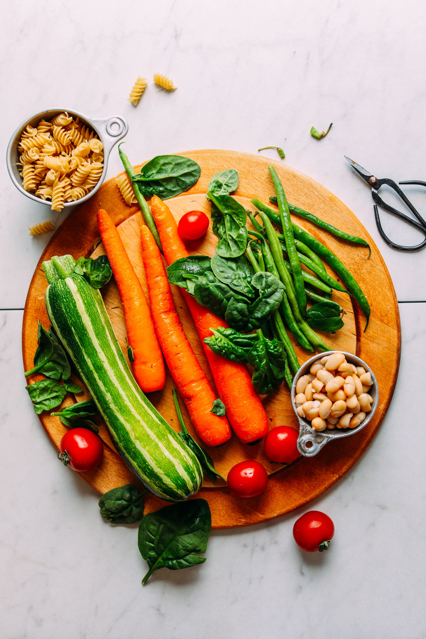 Wood cutting board with zucchini, carrots, spinach, green beans, tomatoes, pasta, and beans for making healthy 1-Pot Vegan Minestrone