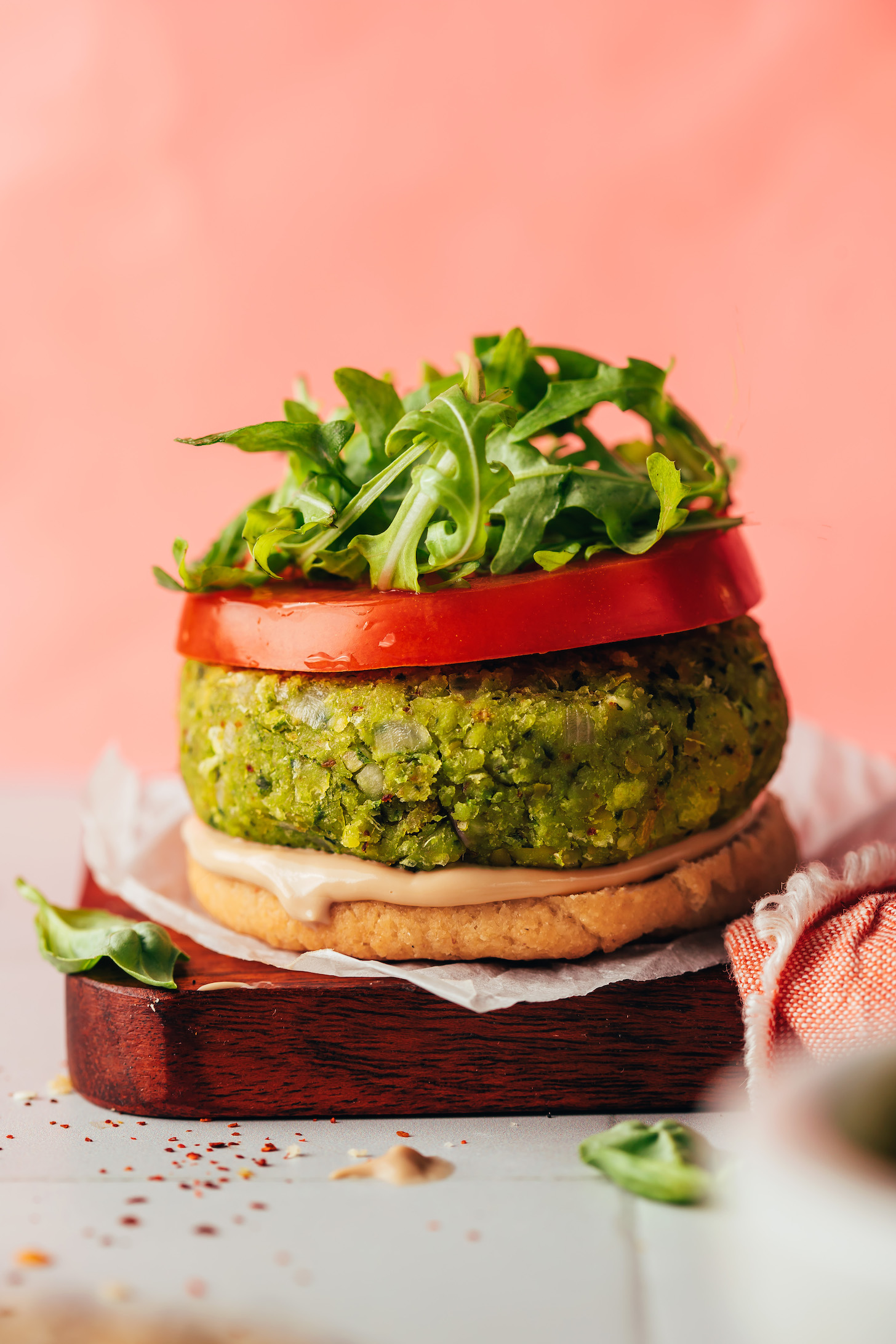 Hamburger bun topped with balsamic aioli, a pesto chickpea burger, tomato slice, and arugula