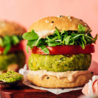 Side view of a pesto veggie burger on a bun with tomato, arugula, and balsamic aioli