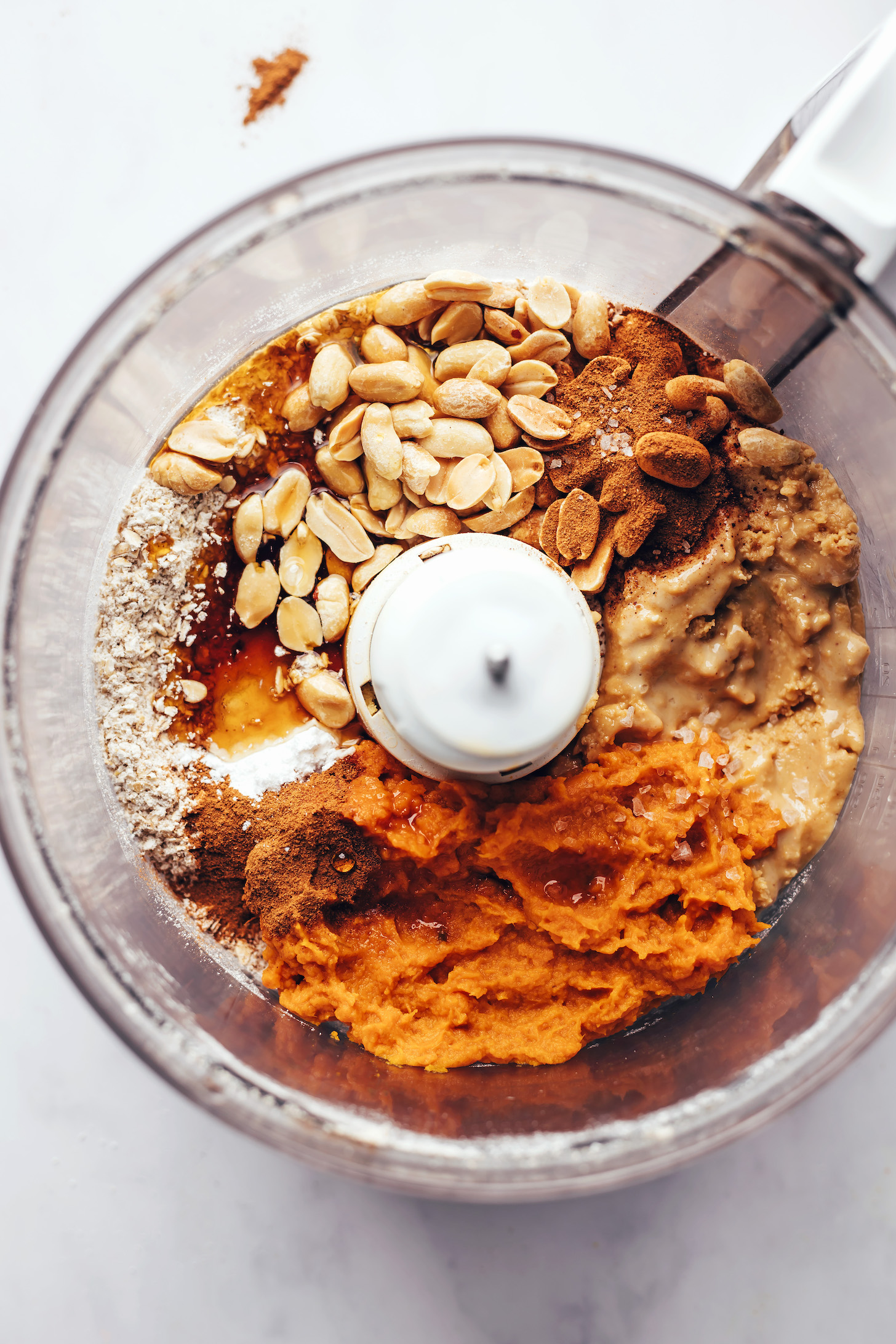 Food processor filled with pumpkin purée, peanut butter, peanuts, cinnamon, salt, oat flour, and baking powder