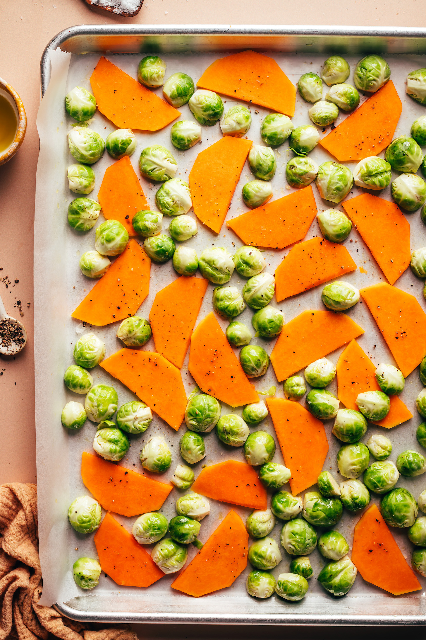 Halved Brussels sprouts and thinly sliced butternut squash on a parchment-lined baking sheet