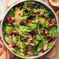 Overhead shot of a vegan chicory green salad with pears, hazelnuts, pepitas, and a lemon vinaigrette