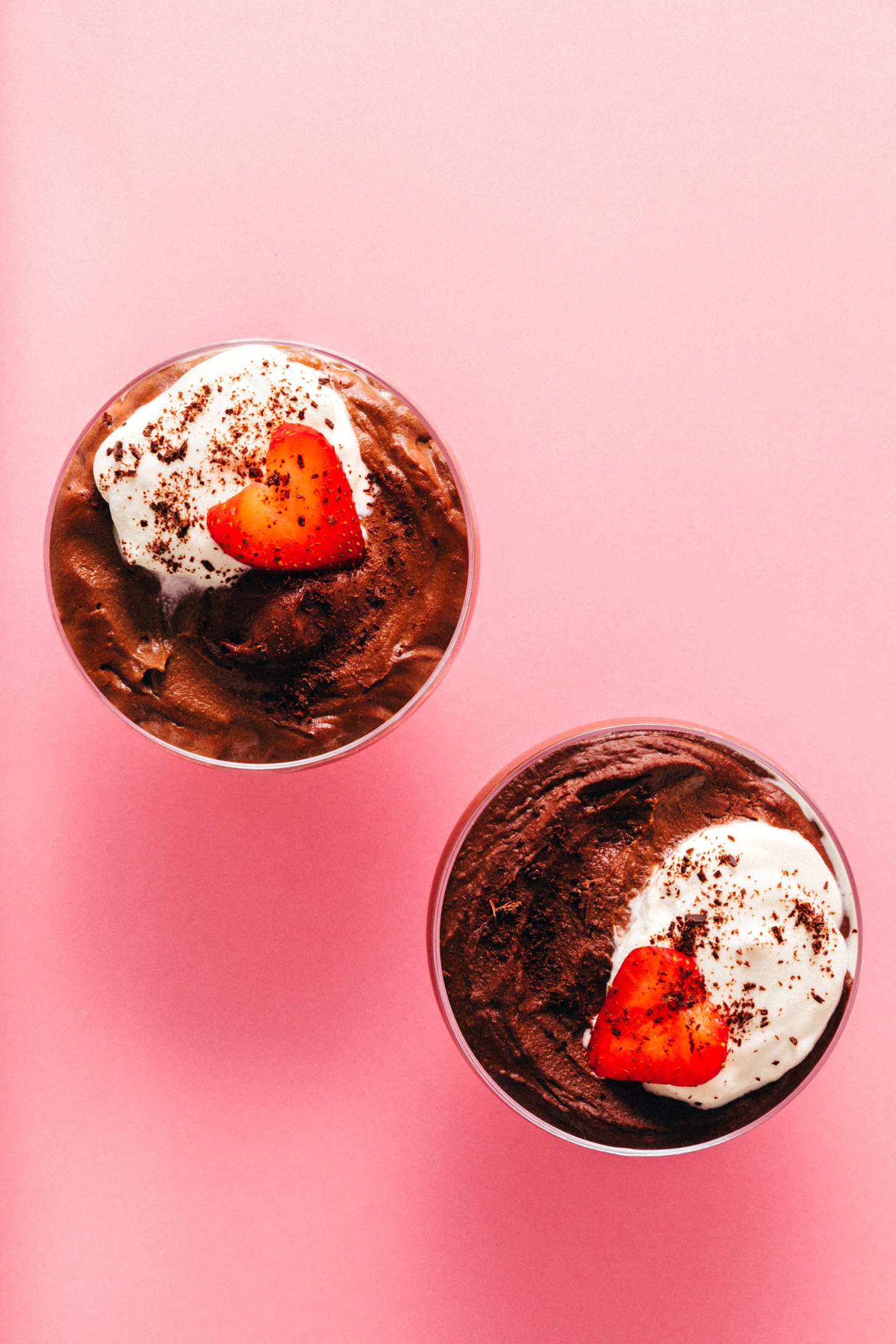 Overhead shot of two bowls of Vegan Chocolate Protein Pudding topped with coconut whipped cream, a strawberry, and shaved chocolate