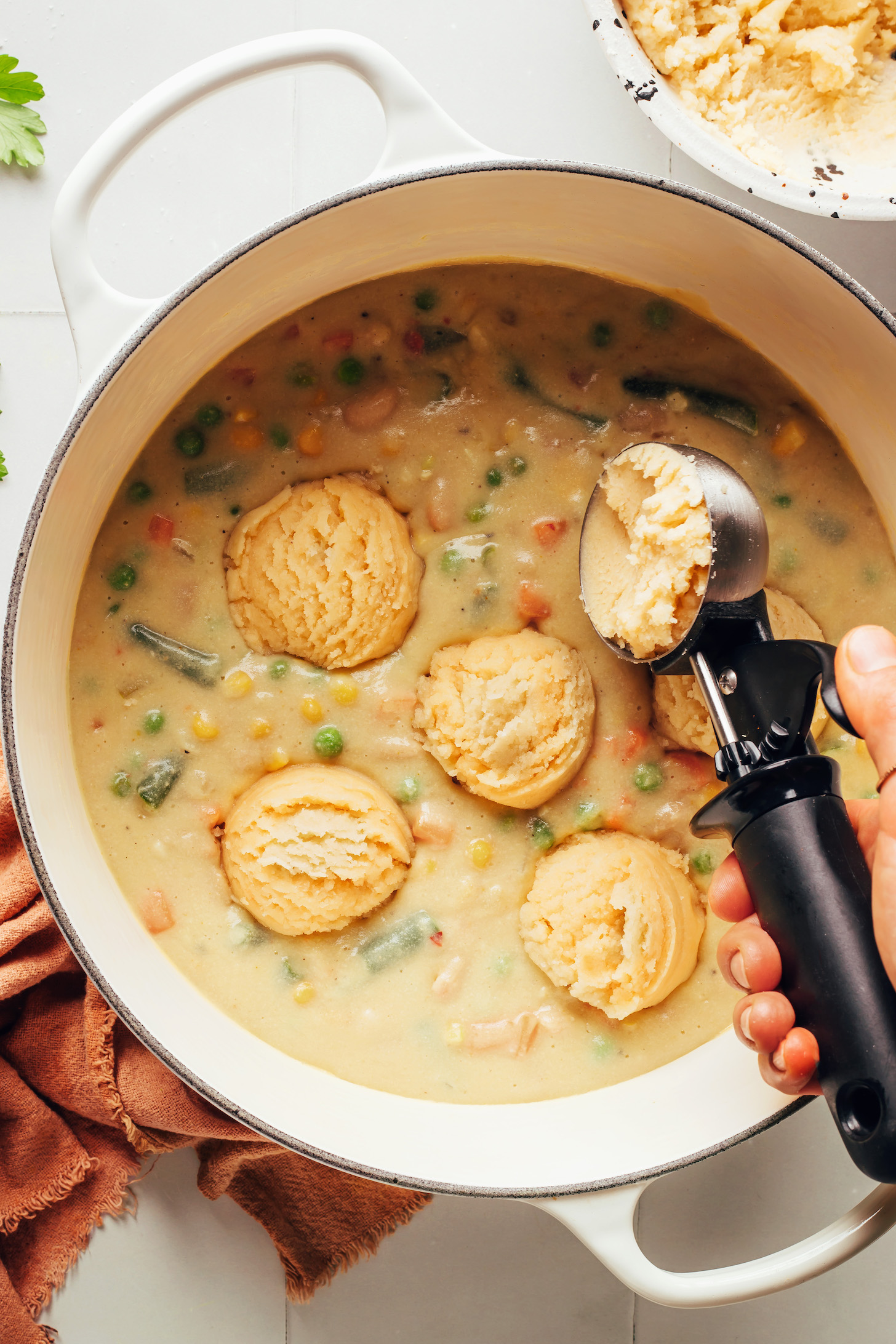 Scooping vegan gluten-free biscuit dough on top of a creamy comforting vegan white bean soup