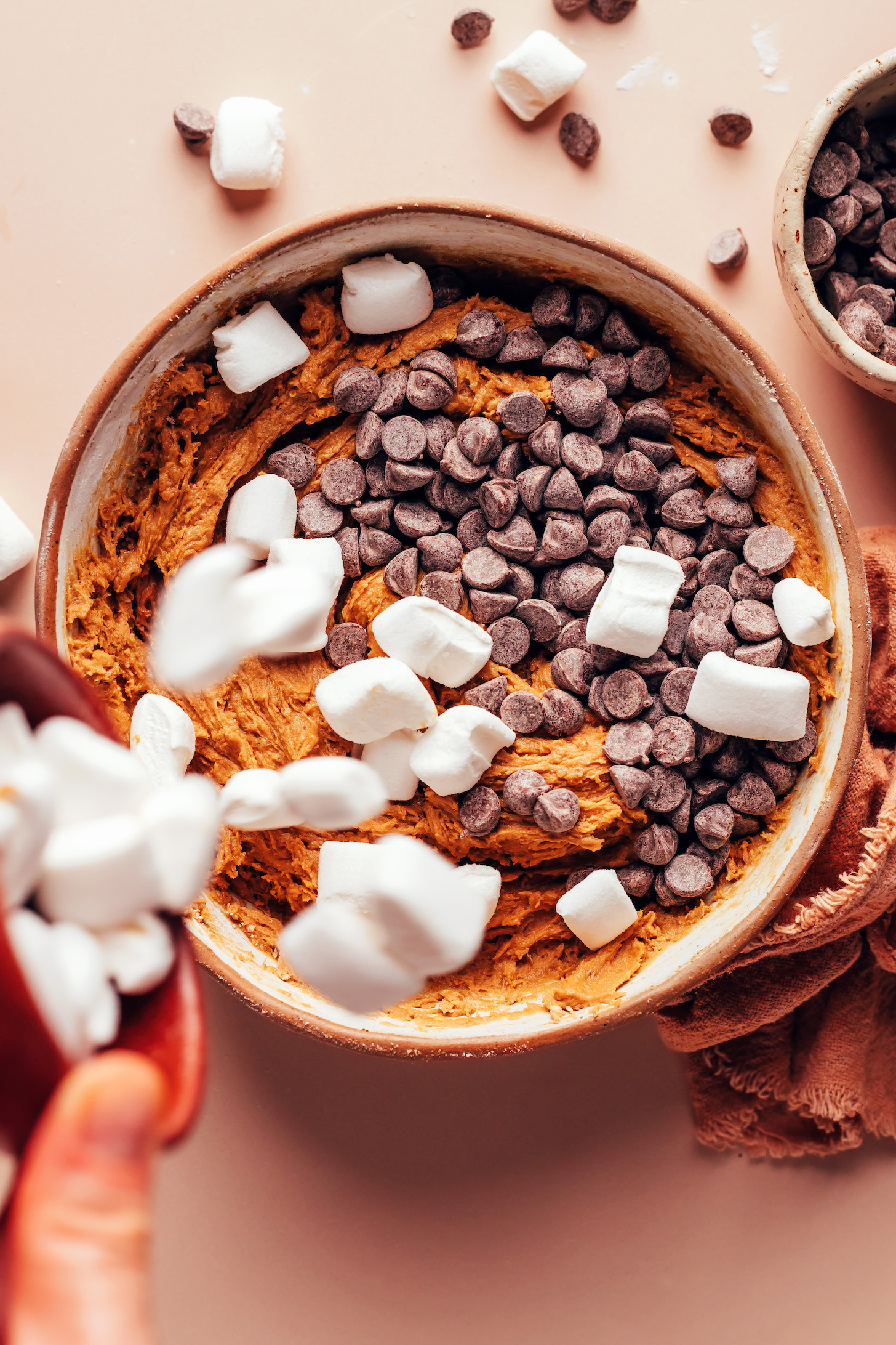 Adding mini marshmallows and chocolate chips to a bowl of s'mores cookie dough